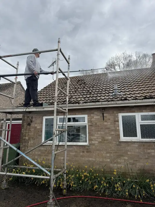 AMK Exteriors technician on scaffold tower cleaning a mossy bungalow roof